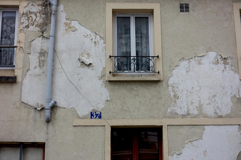 Façade de bâtiment ancien avec enduit écaillé et fenêtre à balustrade.