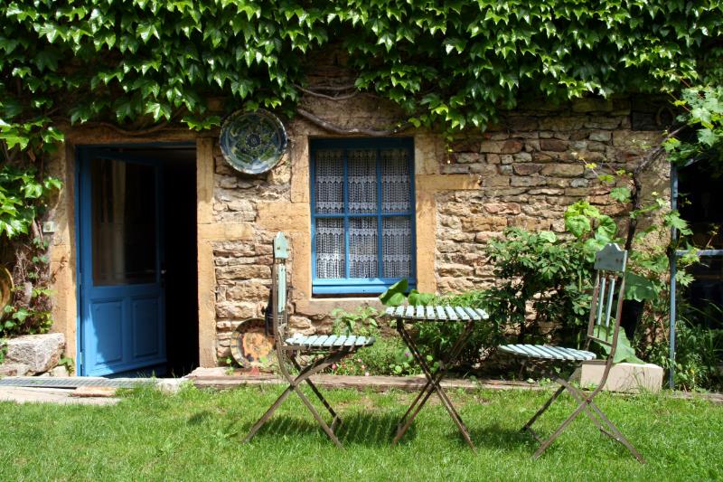 Jardin avec table et chaises de bistro devant une maison en pierre couverte de lierre.
